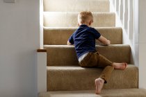 Мальчик, сидящий дома на лестнице, вид сзади. — стоковое фото
