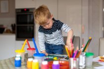 Three year old boy busy painting at home, with paint pots and brushes. — Stock Photo