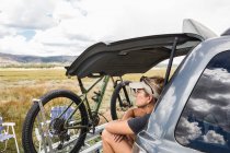Доросла жінка відпочиває на багажнику позашляховика, дивлячись на Віста — стокове фото