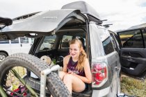 Adolescente sentada na bagageira de um SUV olhando para a vista — Fotografia de Stock