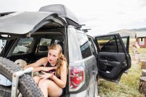 Teenage girl sitting on the tailgate of an SUV looking at vista — Stock Photo