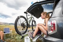 Teenage girl sitting on the tailgate of an SUV looking at vista — Stock Photo