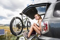 Teenagermädchen sitzt auf der Heckklappe eines Geländewagens und blickt in die Ferne — Stockfoto