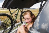 Teenagermädchen sitzt auf der Heckklappe eines Geländewagens und blickt in die Ferne — Stockfoto