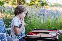 Un niño jugando backgammon al aire libre en un jardín. - foto de stock