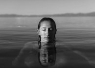 Teenage girl with head above water, eyes closed in calm lake water, black and white — Stock Photo