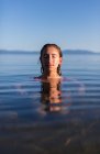 Teenage girl with eyes closed, head and shoulders above the calm water of a lake at dawn — Stock Photo