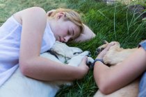 Duas meninas adolescentes deitadas no gramado, abraçando seus cães Golden Retriever. — Fotografia de Stock