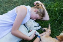 Zwei Teenager-Mädchen liegen auf dem Rasen und umarmen ihre Golden Retriever-Hunde. — Stockfoto