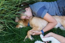 Dos adolescentes tumbadas en el césped, abrazando a sus perros Golden Retriever. - foto de stock