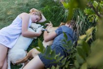 Two teenage girls lying on lawn, hugging their Golden Retriever dogs. — Stock Photo