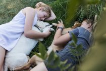 Deux adolescentes allongées sur la pelouse, embrassant leurs chiens Golden Retriever. — Photo de stock