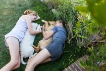 Two teenage girls lying on lawn, hugging their Golden Retriever dogs. — Stock Photo