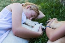 Deux adolescentes allongées sur la pelouse, embrassant leurs chiens Golden Retriever. — Photo de stock