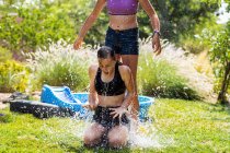Duas adolescentes usando roupa de banho brincando com balões de água em um jardim. — Fotografia de Stock
