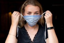 Portrait of young blond woman putting on blue face mask. — Stock Photo