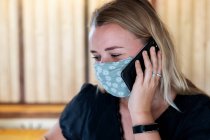 Portrait of young blond woman wearing blue face mask, using mobile phone. — Stock Photo