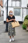 Giovane donna bionda che indossa maschera facciale passeggiando per il villaggio, portando la borsa della spesa. — Foto stock