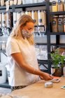 Junge blonde Frau mit Gesichtsmaske kauft in abfallfreiem Vollwertladen ein und macht kontaktloses Bezahlen mit ihrer Kreditkarte. — Stockfoto