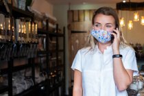 Жінка в масці для обличчя в місцевому магазині, використовуючи мобільний телефон — стокове фото