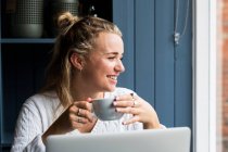 Young blond woman sitting alone at a cafe table with a laptop computer, working remotely. — Stock Photo