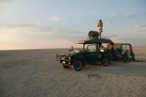 Man standing on top of vehicle parked on the Makadikadi Salt Pans in Botswana. — Stock Photo