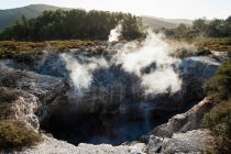 View into a crater with geothermal heat steam rising from the water — Stock Photo