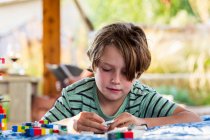 Seven year old boy playing with building blocks on a terrace — Stock Photo