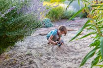 Seven year old boy playing in sandy garden with his toy ship. — Stock Photo