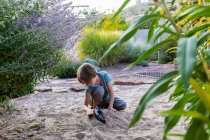 Ragazzo di sette anni che gioca nel giardino sabbioso con la sua nave giocattolo. — Foto stock