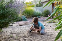 Siebenjähriger Junge spielt mit seinem Spielzeugschiff im Sandgarten. — Stockfoto