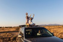 Teenage girl and her younger brother on top of SUV car driving on desert road — Stock Photo
