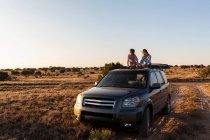 Adolescente chica y su hermano menor en la parte superior de SUV coche de conducción en el camino del desierto - foto de stock