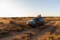 Девочка-подросток и ее младший брат на вершине внедорожника, едущего по пустынной дороге — стоковое фото