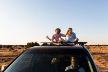 Adolescente et son jeune frère sur le dessus de la voiture SUV conduite sur la route du désert — Photo de stock
