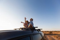 Adolescente y su hermano menor en la parte superior del coche SUV en la carretera del desierto, Cuenca de Galisteo, Santa Fe, NM. - foto de stock