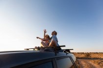 Teenage girl and her younger brother on top of SUV car on desert road, Galisteo Basin, Santa Fe, NM. — Stock Photo
