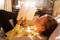 Дівчина-підліток читає книгу вдома в ранковому світлі — стокове фото