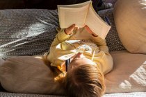 Teenage girl reading book at home in early morning light — Stock Photo