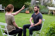 Therapist and client seated in a garden, woman with her hand raised and two fingers extended. — Stock Photo