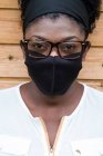 Porträt einer schwarzen Frau mit Brille und Gesichtsmaske, die in die Kamera blickt. — Stockfoto