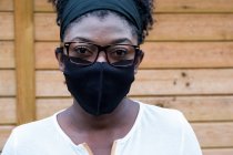 Портрет черной женщины в очках и маске, смотрящей в камеру. — стоковое фото