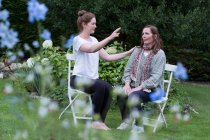 Mujer y terapeuta sentadas en una sesión de terapia alternativa en un jardín. - foto de stock