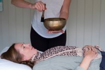 Woman on a couch, and a female therapist using Tibetan singing bowl, sound therapy — Stock Photo