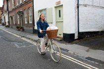 Jovem mulher loira pedalando por uma rua da aldeia. — Fotografia de Stock