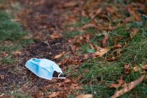 High angle close up of disposed blue surgical face mask lying on ground. — Stock Photo