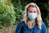 Portrait of young blond woman wearing face mask, looking at camera. — Stock Photo