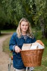Young blond woman on bicycle with basket, smiling at camera. — Stock Photo