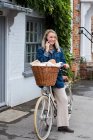 Jeune femme blonde à vélo avec panier, parlant sur téléphone portable. — Photo de stock
