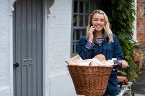 Young blond woman on bicycle with basket, talking on mobile phone. — Stock Photo